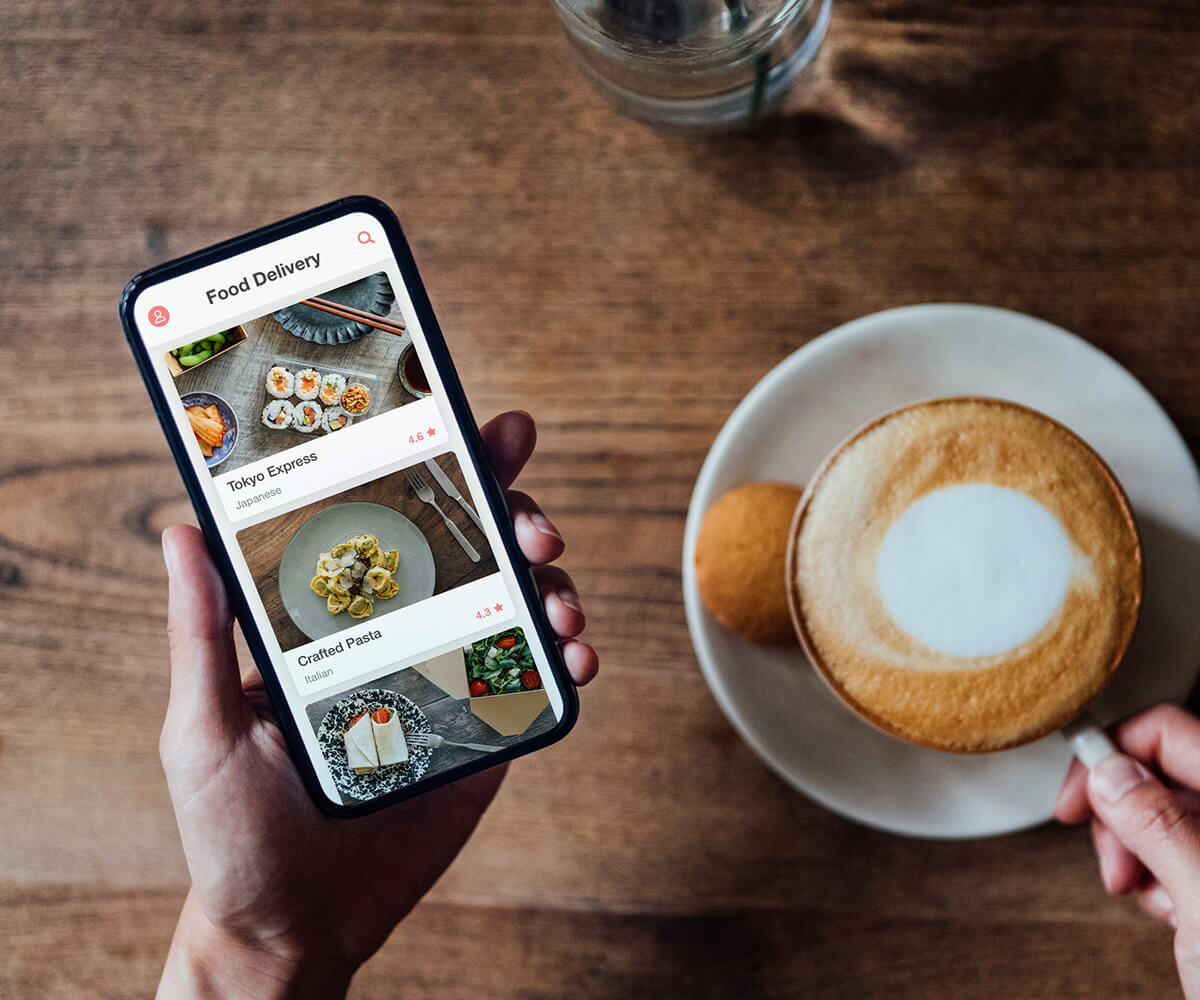 Person browsing a phone delivery app while drinking coffee